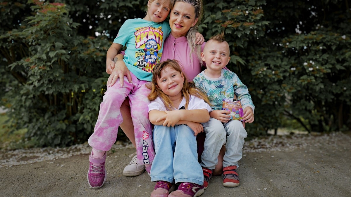 A woman poses with three smiling children outdoors.